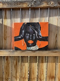 a painting of a black woman hanging on a wooden fence